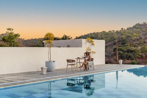a woman sitting at a table next to a pool at ELIVAAS Prive 5 BHK Kvanya Mansion with Pvt Pool & Home Theater in Debāri