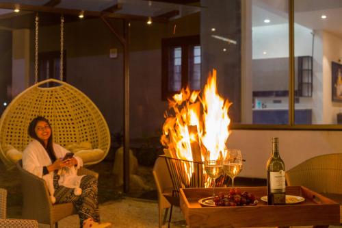 a woman sitting in a chair in front of a fire at ELIVAAS Prive 5 BHK Kvanya Mansion with Pvt Pool & Home Theater in Debāri