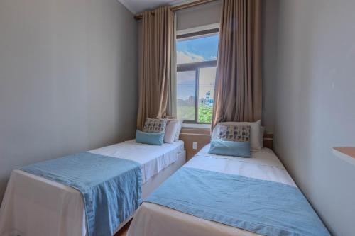 two beds in a room with a window at Hotel Minas Gerais in Poços de Caldas