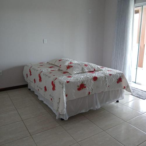 a bed with a white blanket with red flowers on it at Queiroz e Melânia in Penha