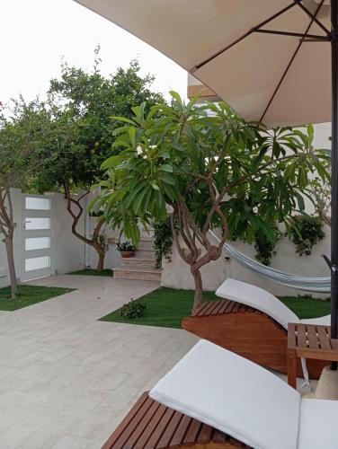 a patio with trees and benches and an umbrella at Casa Vacanze" Almarè" in Marina di Modica