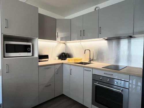 une cuisine avec des armoires blanches et un micro-ondes dans l'établissement Résidence Le Tourmalet - maeva Home - Appartement 2 pièces 8 personnes - Confort MAE-0351, à La Mongie