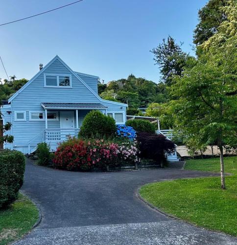a white house with flowers in the driveway at Lake Okareka Calder Road Cottage in Rotorua