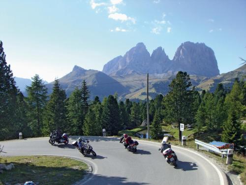 a group of motorcycles driving down a road with mountains at Hotel Gran Paradis in Campitello di Fassa