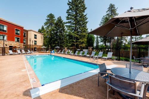 a swimming pool with a table and chairs and an umbrella at TownePlace Suites by Marriott Whitefish Kalispell in Whitefish