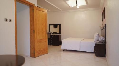a bedroom with a white bed and a wooden door at Hôtel Prestige in Nouadhibou
