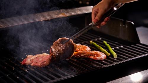 a person cooking meat and vegetables on a grill at 五浦 幽谷隠田跡温泉 Hidden Traces of Rice Terraces Hot Spring - Izura in Kitaibaraki