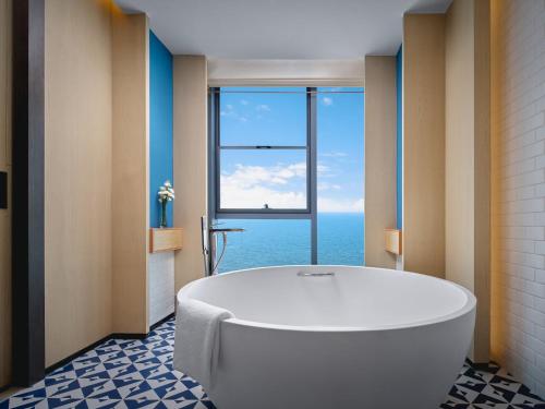 a bathroom with a bath tub and a large window at Hotel Indigo Yantai Golden Coast by IHG in Yantai