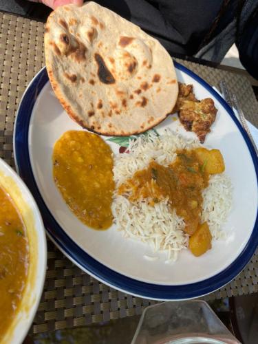 a plate of food with rice and chicken and a bread at Samira's Birds & Butterflies Park-Spashram Ganga Beach Retreat in Rishīkesh