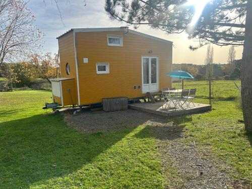 une petite maison jaune avec une table et un parasol dans l'établissement La tiny house Luna, à Villefranche-de-Longchat