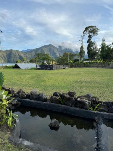 a pond in a park with a field and mountains at La Varuna Kintamani in Kintamani