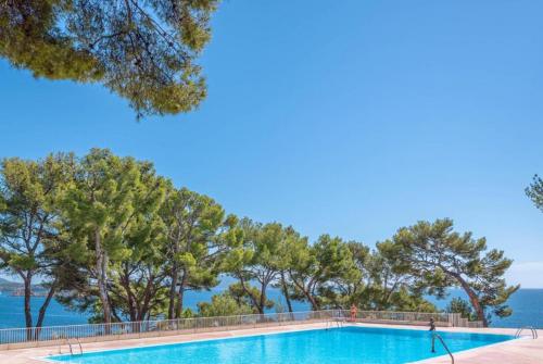 une piscine avec des arbres et l'océan en arrière-plan dans l'établissement Résidence Athéna Port, à Bandol