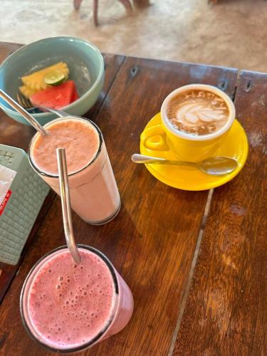 two cups of coffee and a bowl of fruit on a wooden table at Sunny Rose Bungalows Gili Air - Adults only in Gili Air