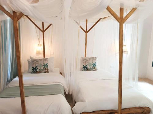 a bedroom with two beds with white sheets and curtains at Peace and Love Garden in Mto wa Mbu