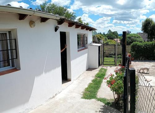 a white house with a black gate and a dog at Casita en las sierras in Huerta Grande