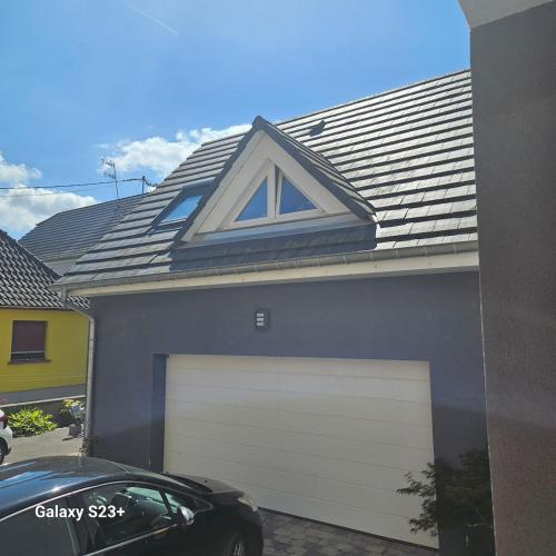 a blue house with a white garage door and a roof at GÎTE LA PERLE - Rossfeld in Rossfeld