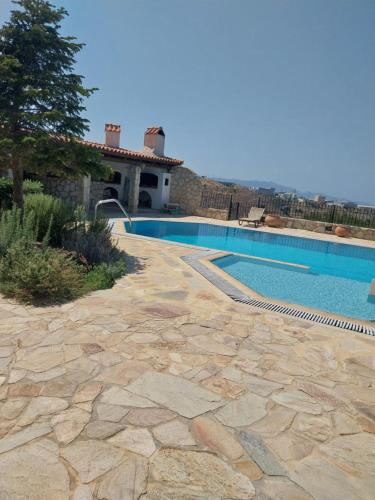 a swimming pool with a stone walkway next to a house at The Three Graces in Karteros
