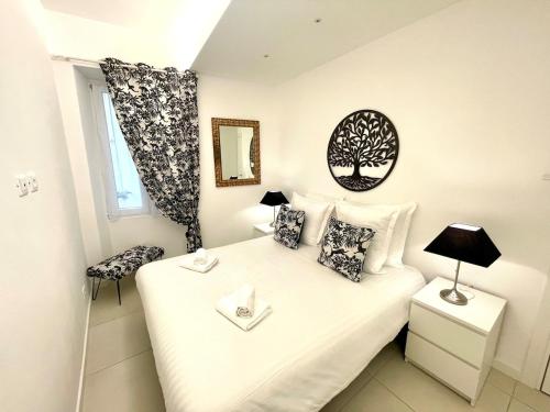 une petite chambre avec un lit avec des draps blancs et des oreillers dans l'établissement Le Cap, beau trois pièces au coeur de la vieille ville, à Menton