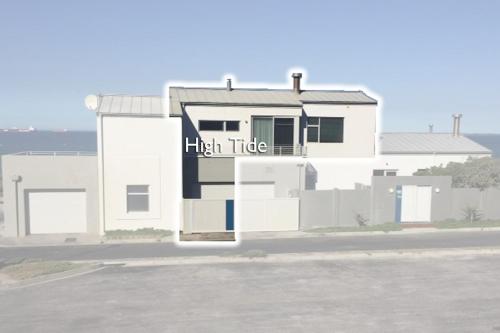 a white house with a high tide sign on it at Bokkombaai in Bloubergstrand