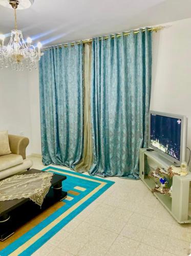 a living room with blue curtains and a television at Home Syrine in Bizerte