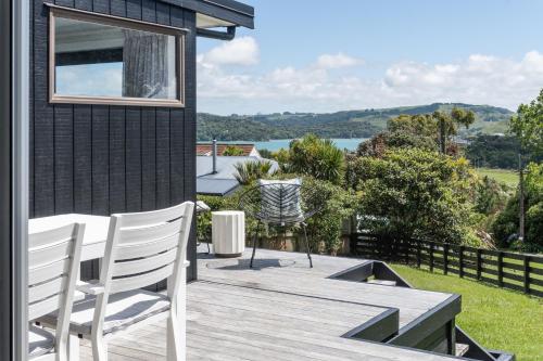una terraza de madera con 2 sillas blancas en una casa en Kotare Cottage, en Raglan