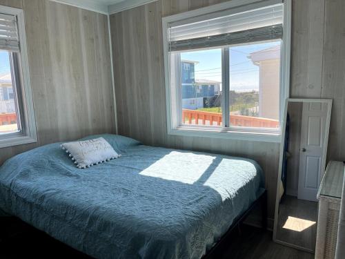 a bedroom with a bed with a blue comforter and two windows at A Drunken Parrots Beach Side Paradise in North Topsail Beach