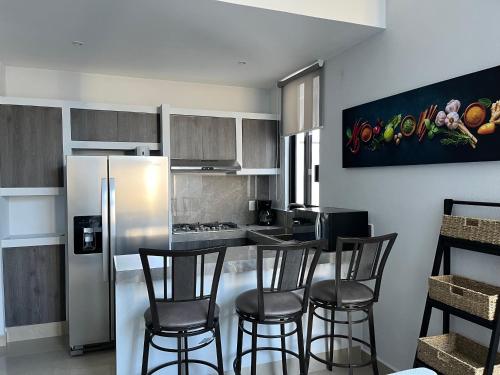 a kitchen with a bar with chairs and a refrigerator at Casa Privada Acapulco in Acapulco