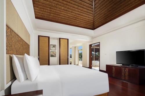 a bedroom with a white bed and a flat screen tv at Grand Mercure Sanya Yalong Bay in Sanya