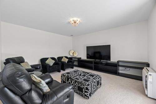 a living room with black leather furniture and a flat screen tv at The Lakeside - Tauranga Holiday Home in Tauranga