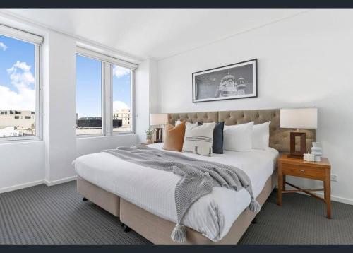a white bedroom with a large bed and two windows at Jolimont Gem - East Melbourne Private Apt - MCG & Rod Laver Arena in Melbourne