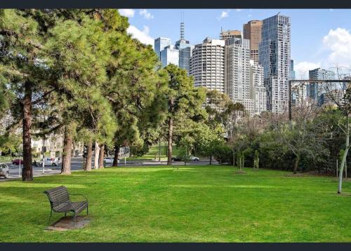 a bench in a park with a city in the background at Jolimont Gem - East Melbourne Private Apt - MCG & Rod Laver Arena in Melbourne