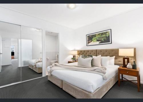 a white bedroom with a large bed and a mirror at Jolimont Gem - East Melbourne Private Apt - MCG & Rod Laver Arena in Melbourne