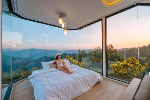 a woman sitting on a bed in a room with windows at Sky View Mon Jam in Chiang Mai