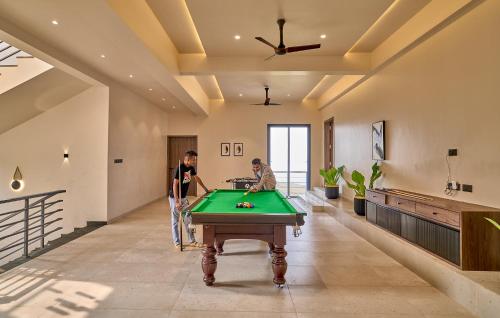 two men playing pool in a room with a pool table at SaffronStays Eldora by the Lake in Matheran