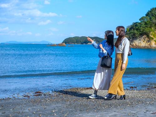 two women standing on the beach looking at the water at 絶景海風癒し庵 新八屋 in Toba