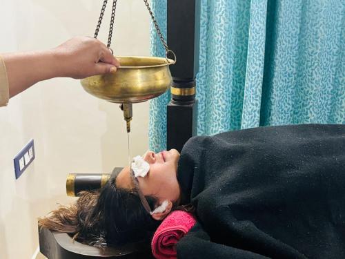 a woman laying on a table with her head in a bowl at Krishnabalram wellness & Ayurveda centre in Rishīkesh