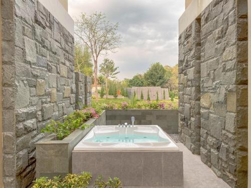 a bath tub in a garden with a stone wall at Shanaya Resort Malang in Malang