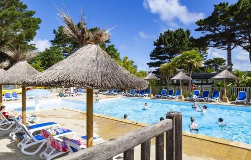 une piscine avec chaises et parasols dans un complexe hôtelier dans l'établissement Domaine Résidentiel de Plein Air Le Port de la Chaine, à Pleubian