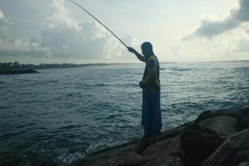 a man standing on the rocks fishing in the ocean at Tomorrowland Beach Villas in Tangalle