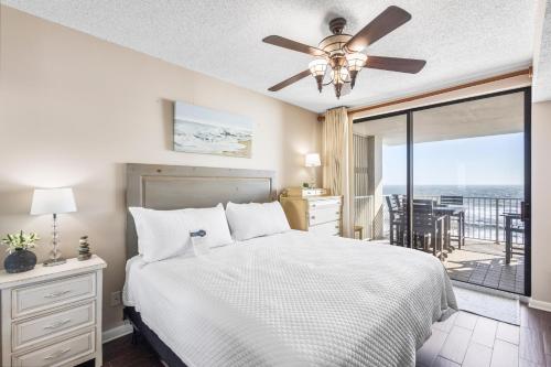 a bedroom with a bed with a ceiling fan and a balcony at Shoalwater 703 by Liquid Life in Orange Beach