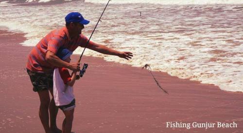 a man with a child holding a fishing rod on the beach at The Gunjur Project Lodge in Gunjur