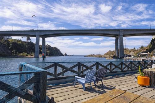 two chairs sitting on a dock near the water under a bridge at H - Cochito in Fort Bragg