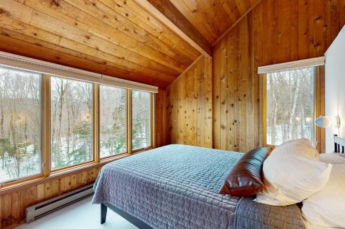 a bedroom with wooden walls and a bed and windows at Mad River Masterpiece in Irasville