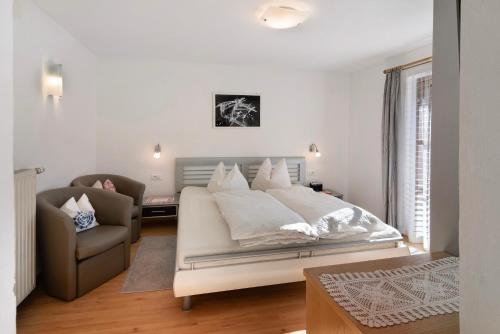 a white bedroom with a bed and a chair at Haus Peer Burgeis in Burgusio