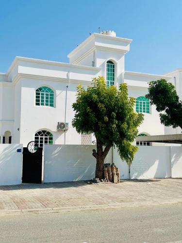 a white building with a tree in front of it at Sukoon Hostel in Muscat