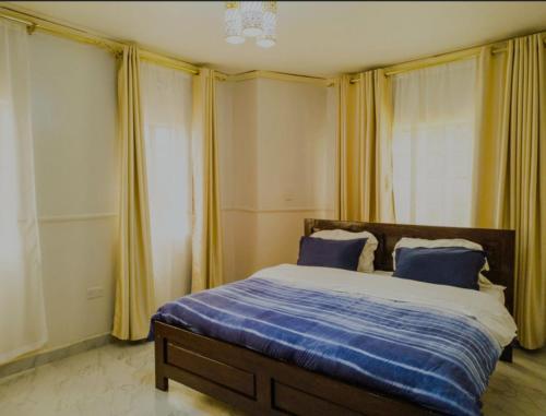 a bedroom with a bed with blue sheets and yellow curtains at Ineza Home in Meru