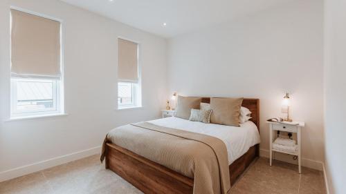 a white bedroom with a bed and two windows at The Piggery in Yarpole