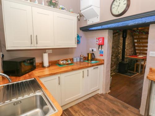 a kitchen with white cabinets and a clock on the wall at Stable Cottage in Pembroke