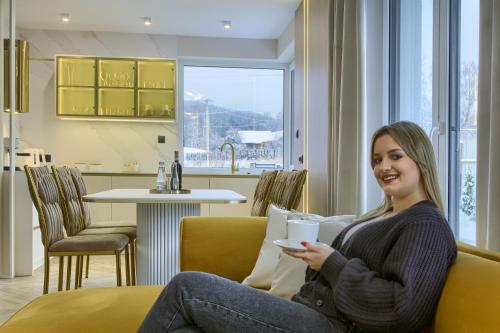 une femme assise sur un canapé tenant une tasse de café dans l'établissement MK Premium Apartamenty, à Tylicz