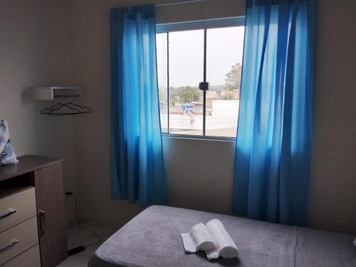 une chambre avec un lit, des rideaux bleus et une fenêtre dans l'établissement Apartamento Praia do Sonho- CasaMora, à Palhoça